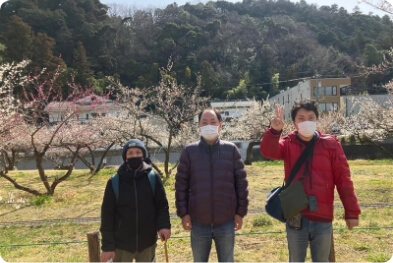 満開の梅畑の前で記念写真をとっている3人の利用者さん